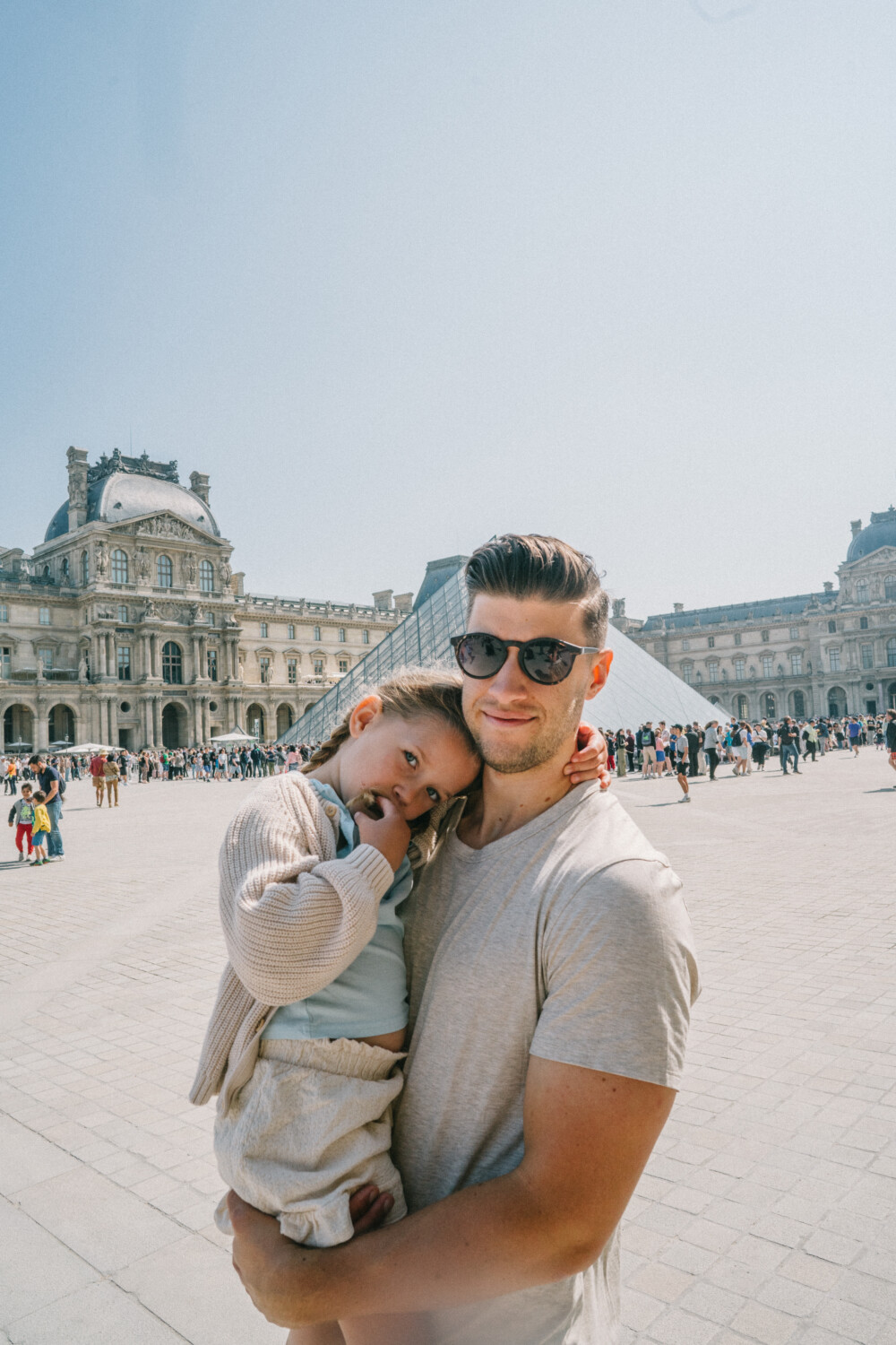 man carrying her child and taking a photo near the Louvre 