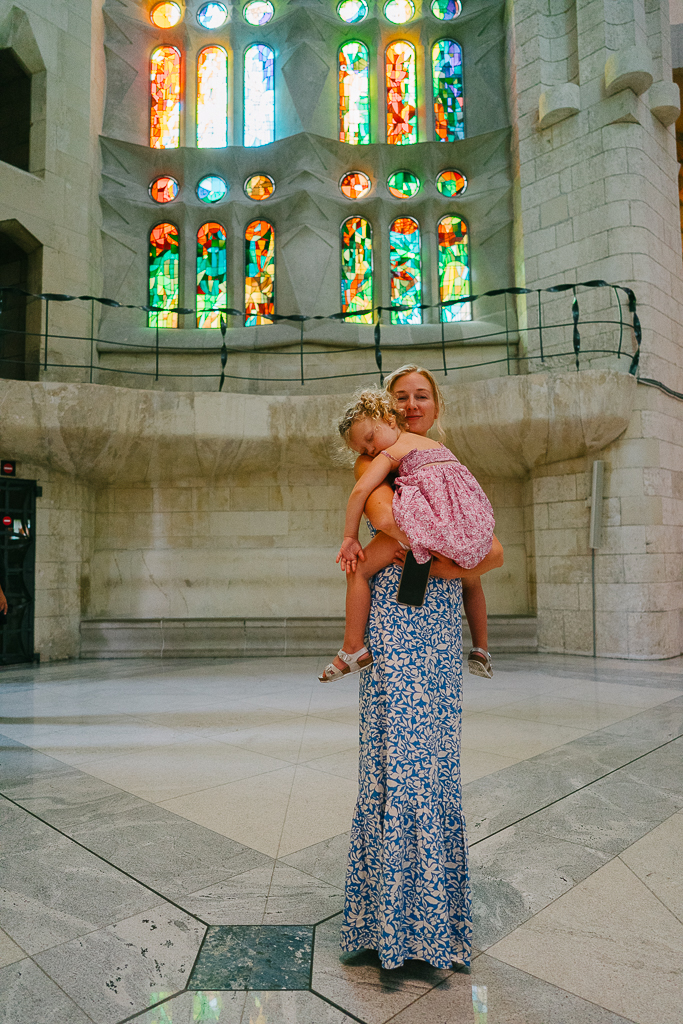 Ruth Nuss holding her daughter and wearing a blue maxi dress in La Sagrada Familia for her Spain and Portugal outfits