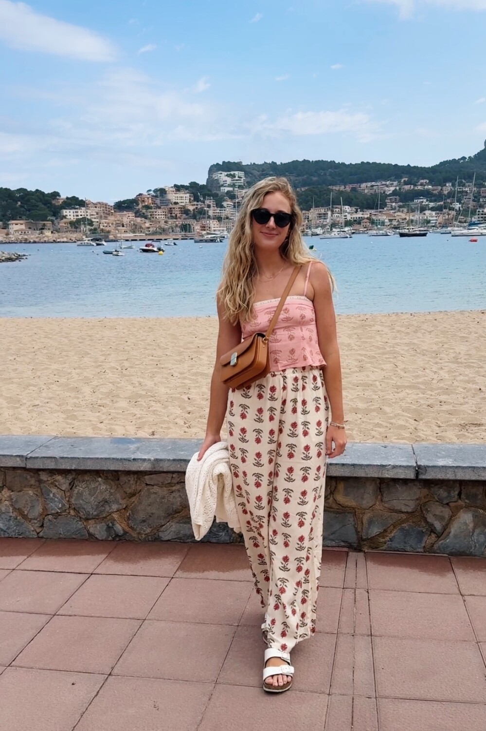 Ruth Nuss wearing white floral pants and a pink top on a beach in Mallorca for her Spain and Portugal outfits