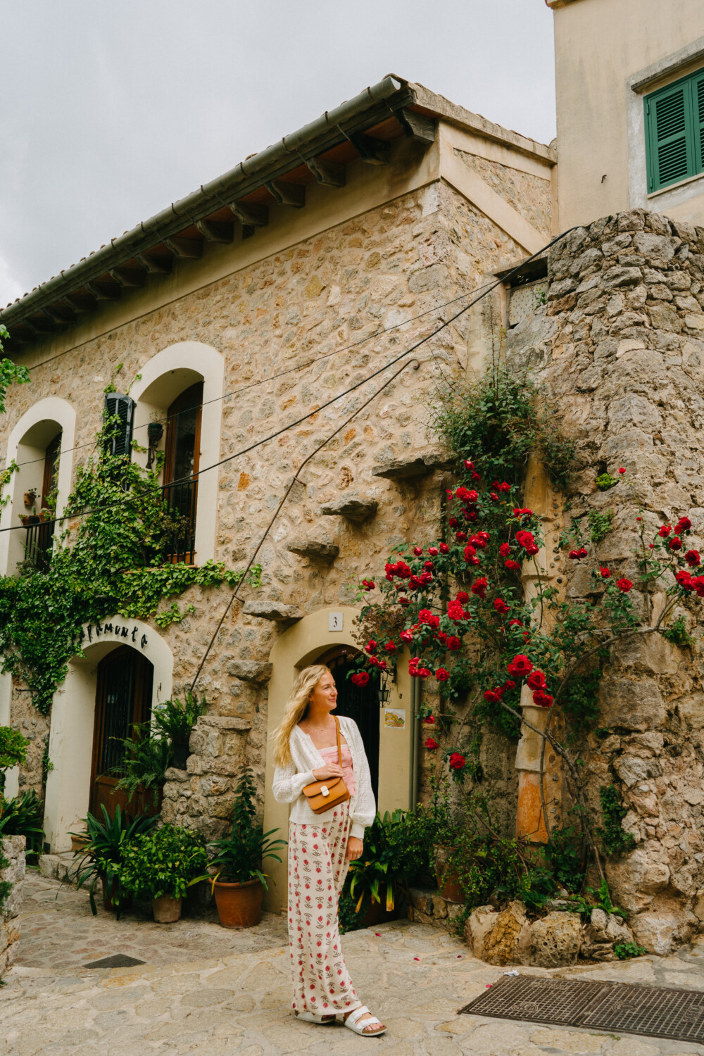 ruth nuss standing against a stone wall with red flowers in Valldemossa, mallorca