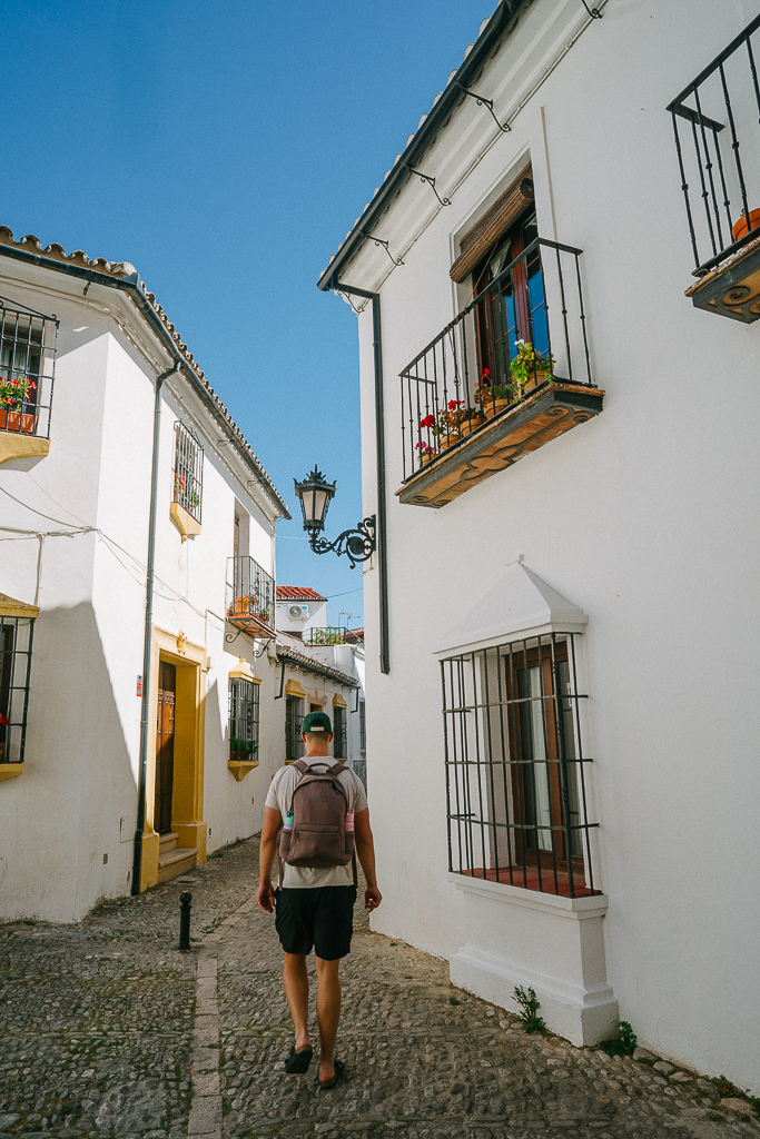 Tyler Nuss walking between white buildings on cobblestones in ronda spain