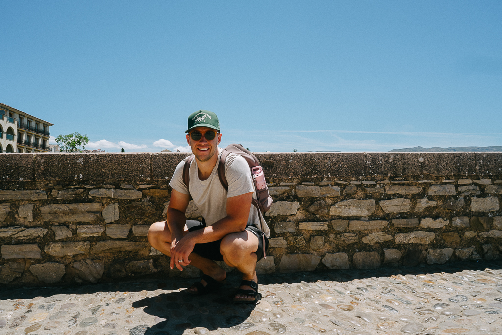 man smiling next to a stone wal