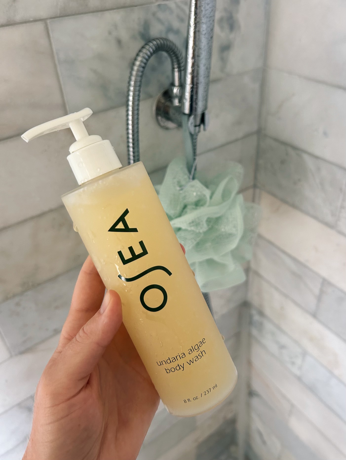 osea body wash in a shower next to a mint green loofah