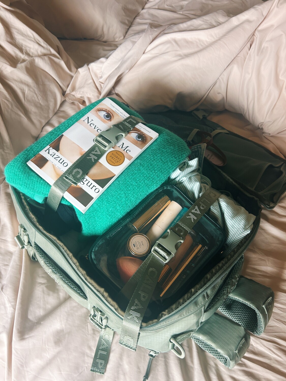 a book, sweater, and cosmetic case packed into the calpak terra backpack