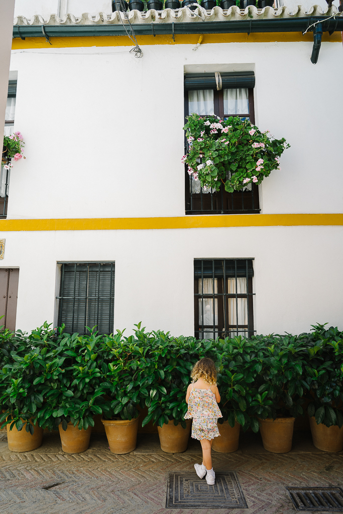 little girl standing in front of bushes and a white building in sevilla spain