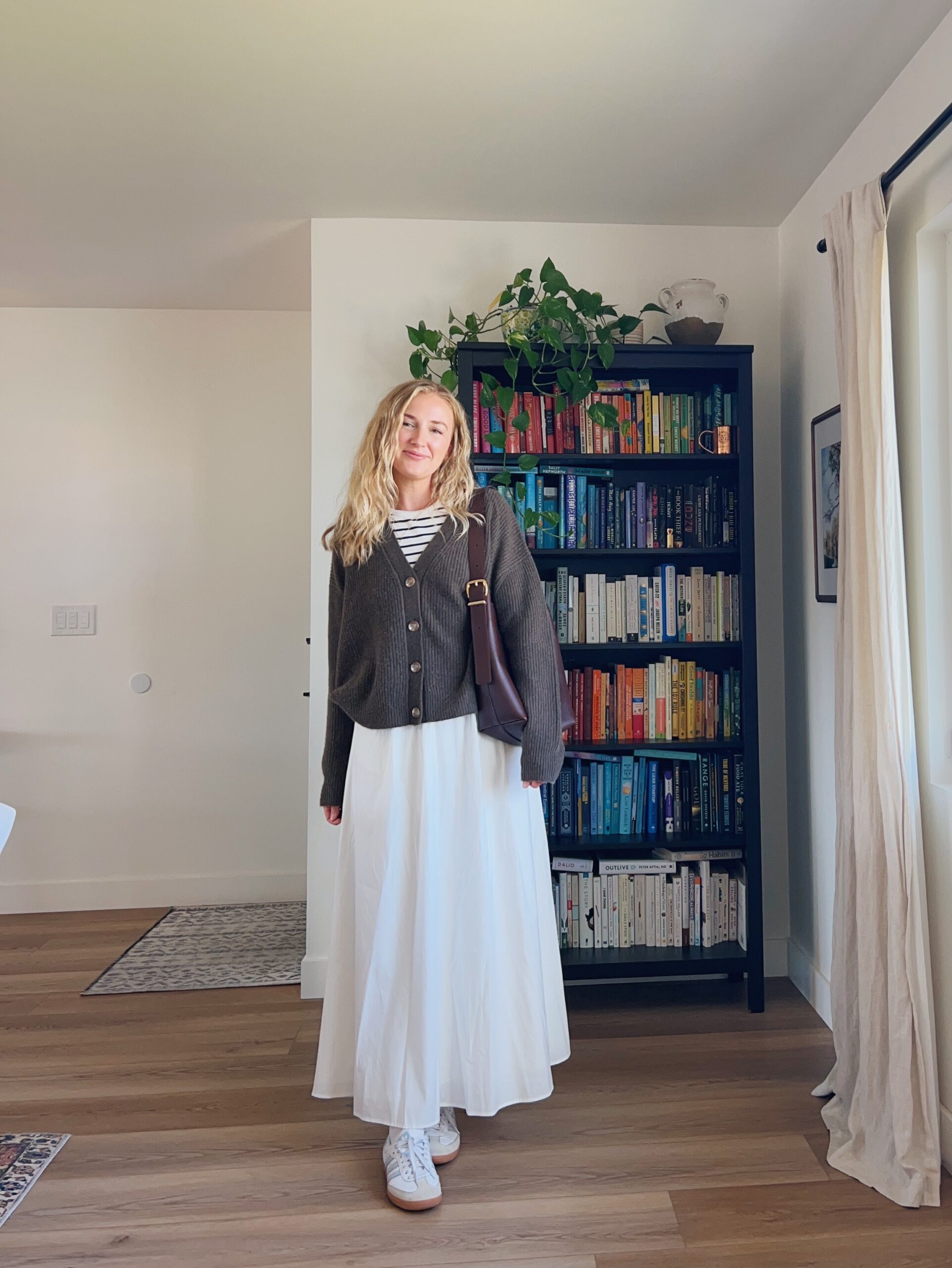 Ruth Nuss wearing a white maxi skirt outfit idea with a striped tank top and a brown vneck cardigan