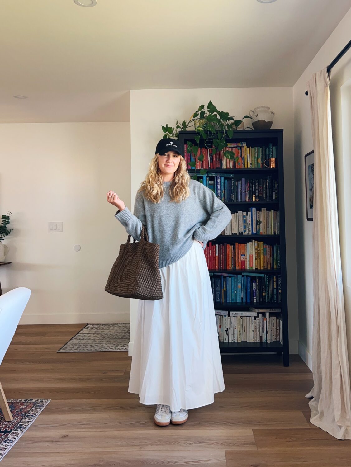 white maxi skirt outfit ideas. ruth nuss wearing a white maxi skirt, gray sweater, and a baseball cap.