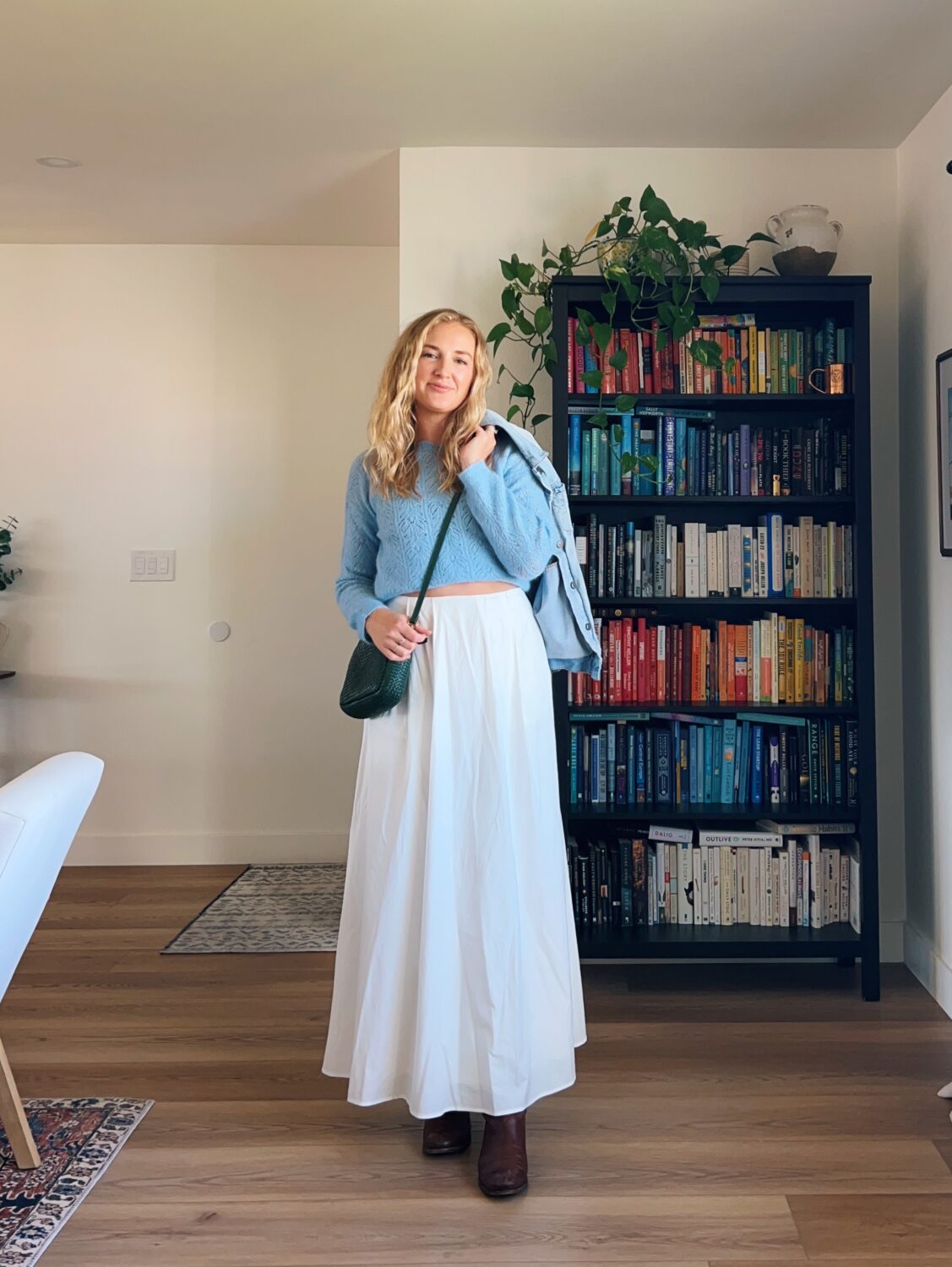 ruth nuss wearing a white maxi skirt outfit idea and her light blue sweater, green crossbody purse, and brown boots.