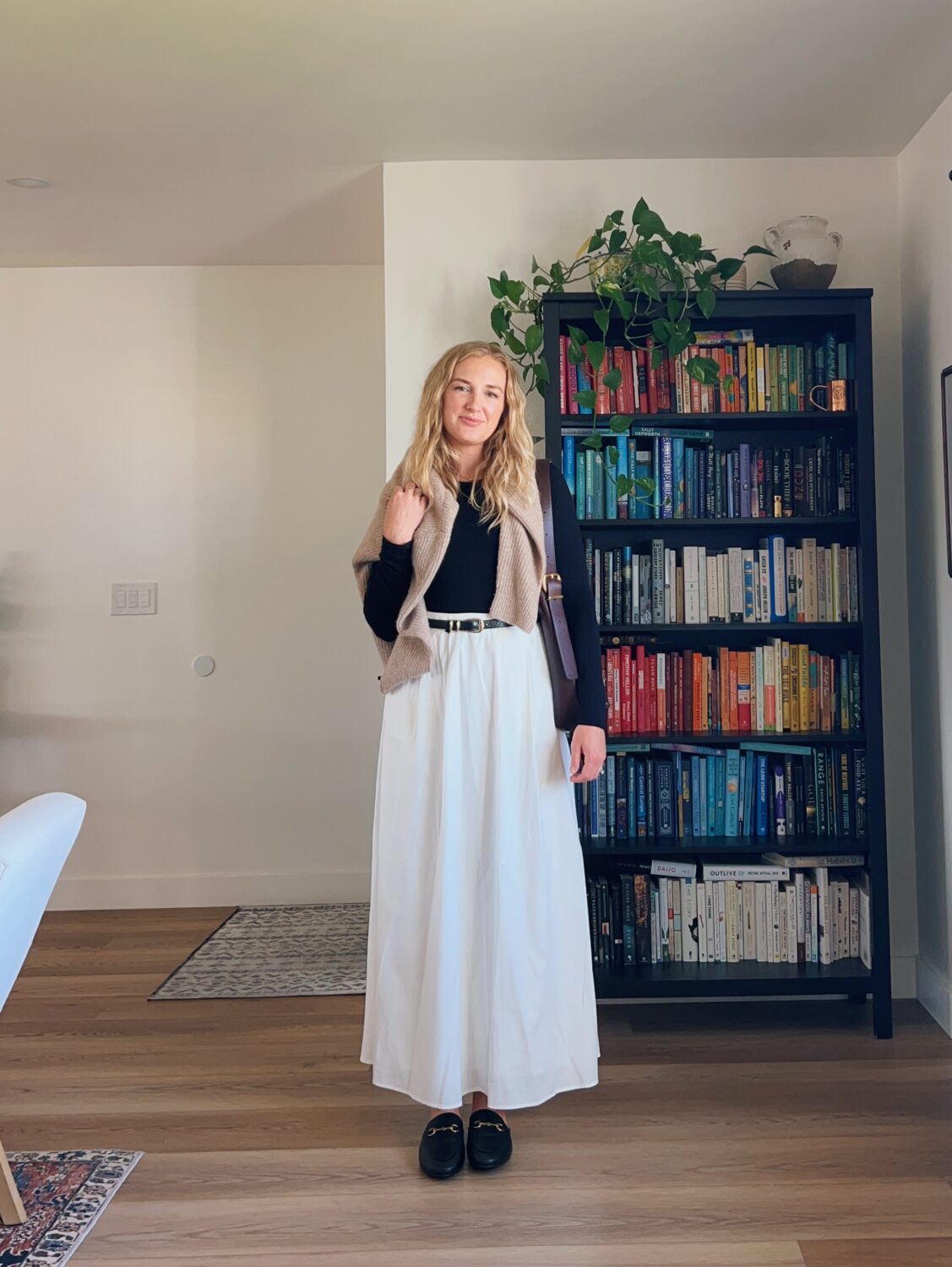 Ruth Nuss wearing a black bodysuit, white maxi skirt, black mules, and an oatmeal sweater over her shoulders.