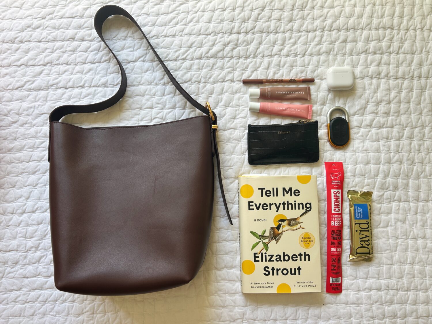 madewell bucket tote on a bed next to a book, snacks, keys, wallet, and airpods