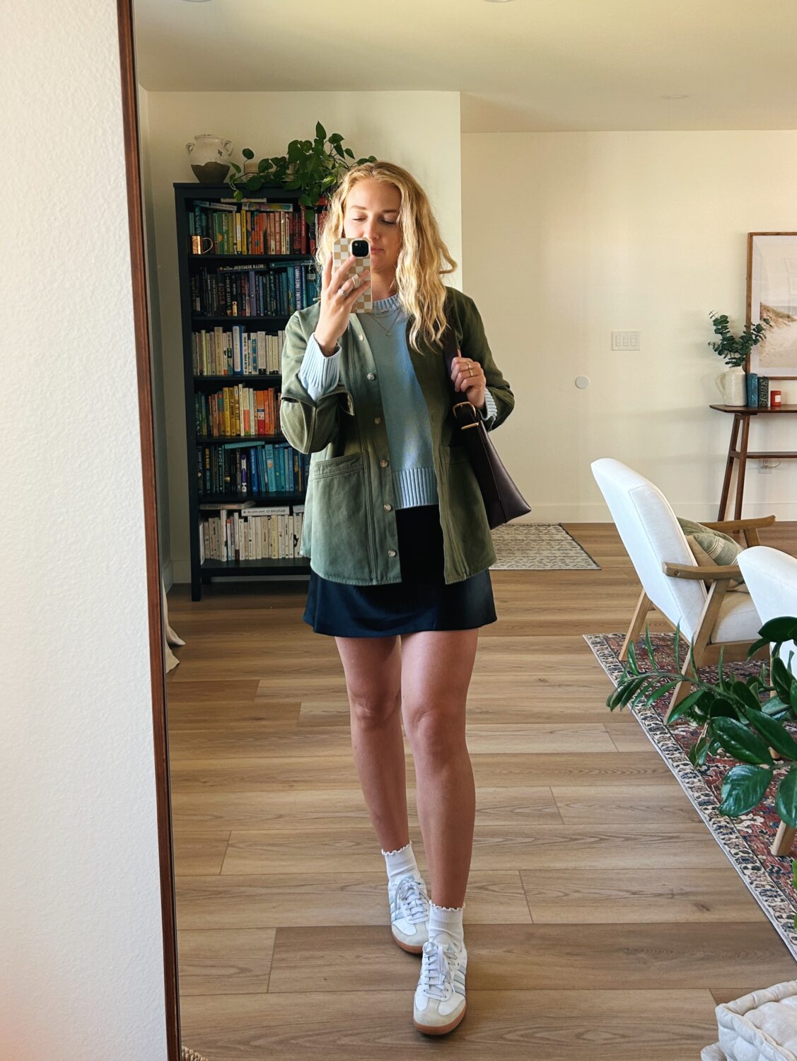 ruth nuss wearing a blue sweater, black skirt, and a green sezane will jacket